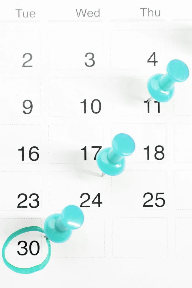 Zu sehen sind ein Paar Hände mit blauen Latexhandschuhen vor einem weißen Hintergrund. Die Hände bilden mit den Fingern ein Herz, wobei die Daumen die untere Spitze bilden. Die gebräunten Unterarme des Models sind ebenfalls zu erkennen.